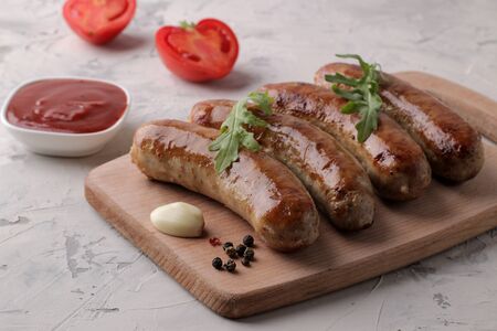 Grilled sausages with a variety of vegetables tomatoes and garlic, red sauce and spices on a light background.の写真素材