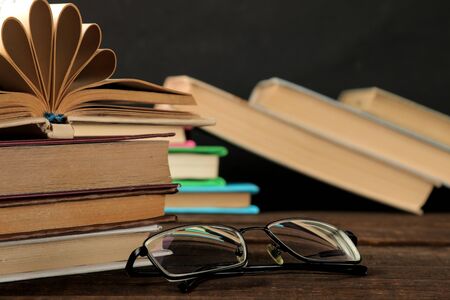 A stack of books and glasses on a brown wooden table and on a black background. Old books. Education. school. studyの写真素材