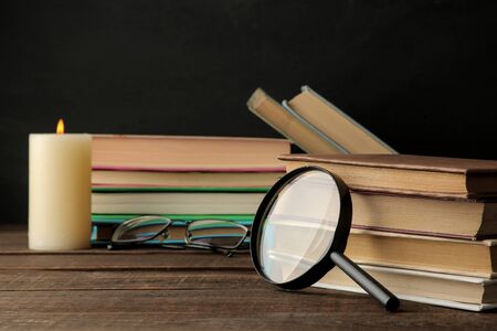 A stack of books and a magnifier on a brown wooden table and on a black background. Old books. Education. school. studyの写真素材