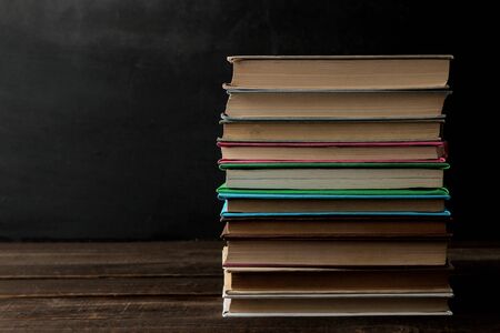 A stack of books on a brown wooden table and on a black background. Old books. Education. school. study With space for inscriptionsの写真素材