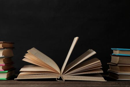 Books and unfolded book on a brown wooden table and on a black background. Old books. Education. school. studyの写真素材