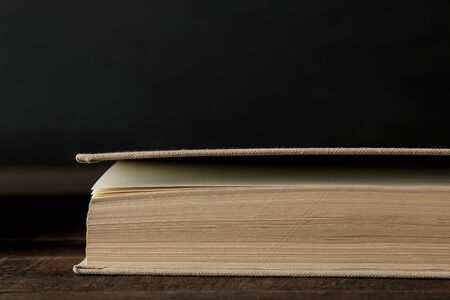 The expanded book close on a brown wooden table and on a black background. Old books. Education. school. study...の写真素材