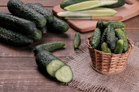 Fresh green cucumbers in a basket and slices of cucumbers on a brown wooden table. vegetablesの写真素材
