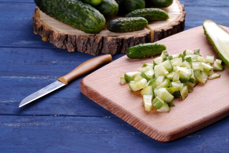 Lots of chopped cucumber slices on a cutting board with a knife on a blue wooden tableの写真素材
