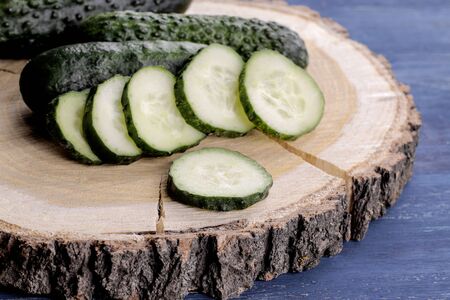 Fresh cucumbers. Sliced cucumber on a wooden stand on a blue wooden tableの写真素材