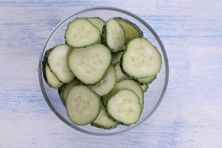 Slices of fresh cucumber in a glass bowl on a blue wooden table. view from aboveの写真素材