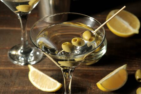 Martini in a glass wineglass with green olives on a skewer on a brown wooden table. cocktails. barの写真素材