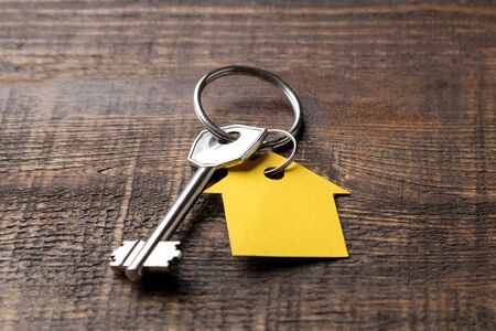 The concept of buying a home. Keys with keychain house on a brown wooden background close-up.の写真素材