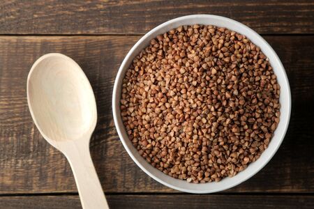 Dry buckwheat groats in a white bowl with a spoon on a wooden brown table. cereals. healthy food. porridge. top viewの写真素材