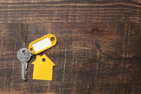The concept of buying a home. Keys with a keychain and a house on a brown wooden background. top view with space for inscriptionの写真素材