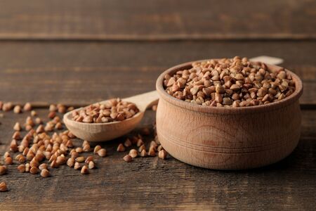 Dry buckwheat groats in a wooden bowl and spoon on a wooden brown table. cereals. healthy food. porridge.の写真素材