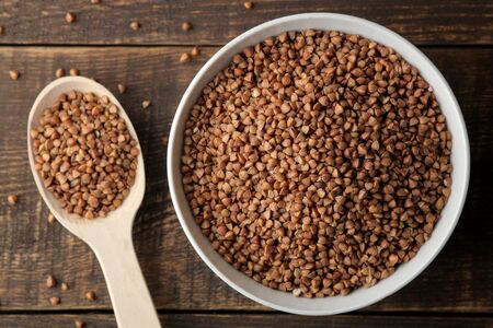 Dry buckwheat groats in a white bowl with a spoon on a wooden brown table. cereals. healthy food. porridge. top viewの写真素材