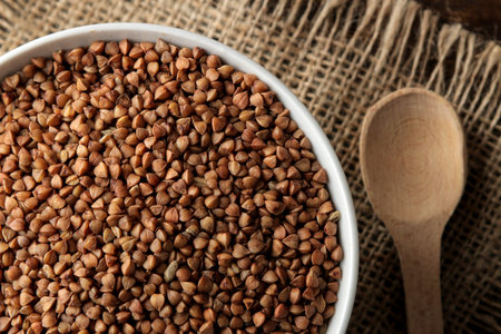 Dry buckwheat groats in a white bowl with a spoon on a wooden brown table. cereals. healthy food....