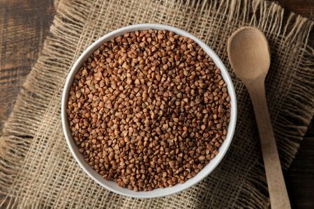 Dry buckwheat groats in a white bowl with a spoon on a wooden brown table. cereals. healthy food. porridge. top viewの写真素材