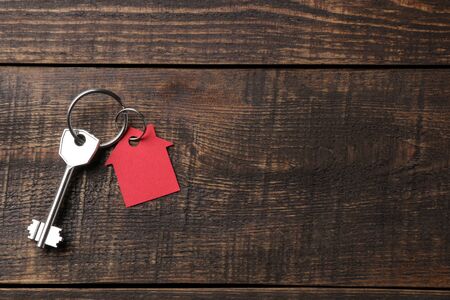 The concept of buying a home. Keys with keychain house on a brown wooden background. view from above. with space for inscriptionの写真素材