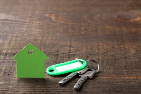 The concept of buying a home. Keys with a keychain and a house on a brown wooden background. with space for inscriptionの写真素材
