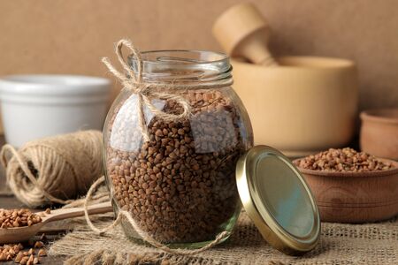 Dry buckwheat groats in a glass jar in the foreground on a wooden brown table. cereals. healthy food. porridge.の写真素材
