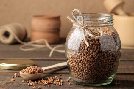 Dry buckwheat groats in a glass jar in the foreground on a wooden brown table. cereals. healthy food. porridge.の写真素材