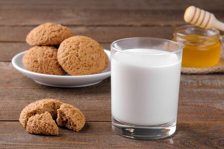 Tasty oatmeal cookies with honey and milk on a napkin on a brown wooden tableの写真素材