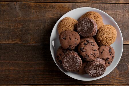 different tasty cookies on a plate on a brown wooden table. top view with space for inscriptionの写真素材