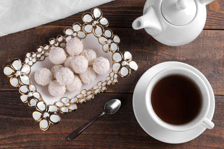 Tasty sweet coconut candies in a vase with tea on a brown wooden table. view from aboveの写真素材
