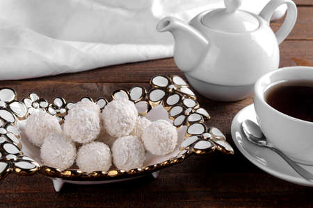 Tasty sweet coconut candies in a vase with tea on a brown wooden table.の写真素材
