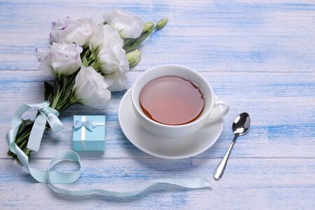 Beautiful white flowers. Eustoma bouquet with tea and gift on a blue wooden table.の写真素材