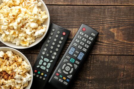 Popcorn and TV remote on a brown wooden background. concept of watching movies at home. view from aboveの写真素材