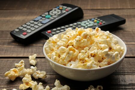 Popcorn and TV remote on a brown wooden background. concept of watching movies at home.の写真素材