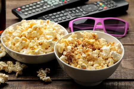 Popcorn, 3D glasses and TV remote on a brown wooden background. concept of watching movies at home.の写真素材