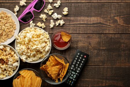 Popcorn and various snacks, 3D glasses, TV remote on a brown wooden background. concept of watching movies at home. view from aboveの写真素材