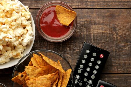 Popcorn and various snacks, TV remote on a brown wooden background. concept of watching movies at home. view from aboveの写真素材