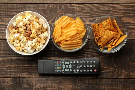 Tortilla popcorn, chips and TV remote on a brown wooden background. concept of watching movies at home. view from aboveの写真素材