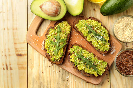 Avocado and arugula sandwiches and other ingredients on a natural wooden table. Sandwich with avocado puree. view from aboveの写真素材