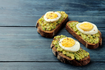 Sandwich with avocado puree and egg on a blue wooden table with space for text.