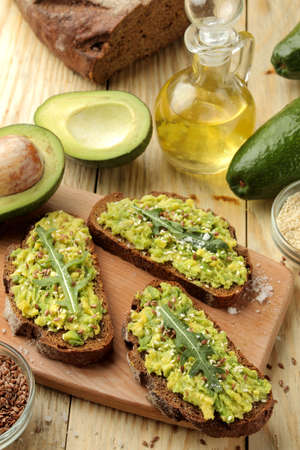 Avocado and arugula sandwiches and other ingredients on a natural wooden table. Sandwich with avocado puree.の写真素材