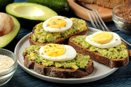 Sandwich with avocado puree and egg on a plate and ingredients for cooking on a blue wooden table.