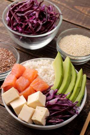 poke bowl Hawaiian food. a plate with rice, salmon, avocado, cabbage and cheese, near sesame. on a brown wooden table.の写真素材