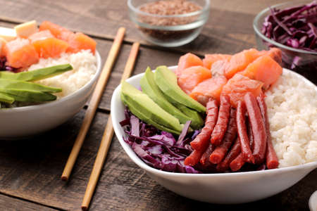 poke bowl Hawaiian food. a plate of rice, salmon, avocado, cabbage and cheese, next to sesame and soy sauce. on a brown wooden table.の写真素材