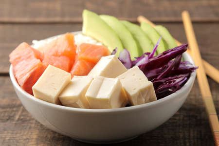 poke bowl Hawaiian food. plate with rice, salmon, avocado, cabbage and cheese, on a brown wooden tableの写真素材