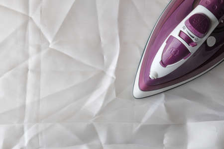 Lilac iron on a piece of white crumpled fabric. ironing clothes. household electrical appliances. view from above.の写真素材