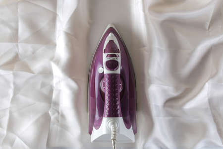 Lilac iron on a piece of white crumpled fabric. ironing clothes. household electrical appliances. view from above.の写真素材