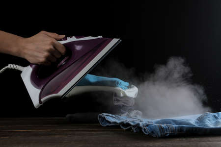 The girl lets steam of lilac iron on clothes on a black background. ironing clothes. household electrical appliances.の写真素材