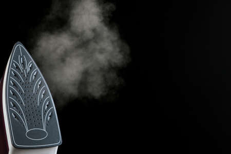 Lilac iron releases steam on a black background. ironing clothes. household electrical appliances. with space for textの写真素材