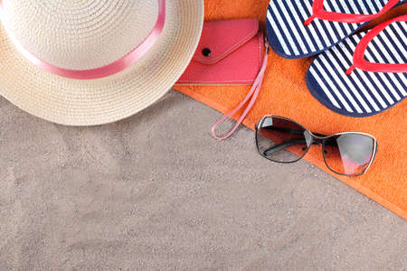 Beach accessories. Flip-flops, hat and glasses on an orange towel on the sea sand. Top viewの写真素材