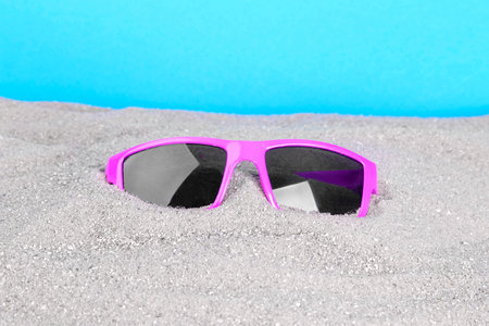 pink sunglasses in the sand close-up on a blue backgroundの写真素材