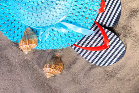 beach accessories. Flip-flops, a hat and seashells on the sand of the sea. Top viewの写真素材