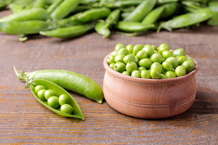 Fresh green peas in a wooden bowl in the background on a brown wooden backgroundの写真素材