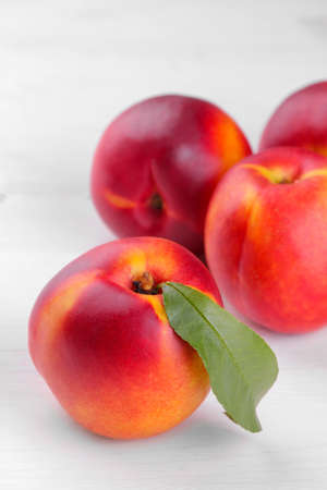 Ripe large nectarines with a green leaf close-up on a white wooden backgroundの写真素材
