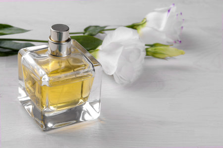 Vial of perfume and beautiful white flowers of eustoma on a white wooden background